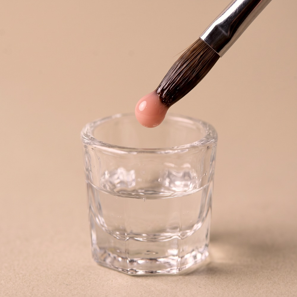 Pincel de acrílico con una perla de producto sobre un vaso de monómero