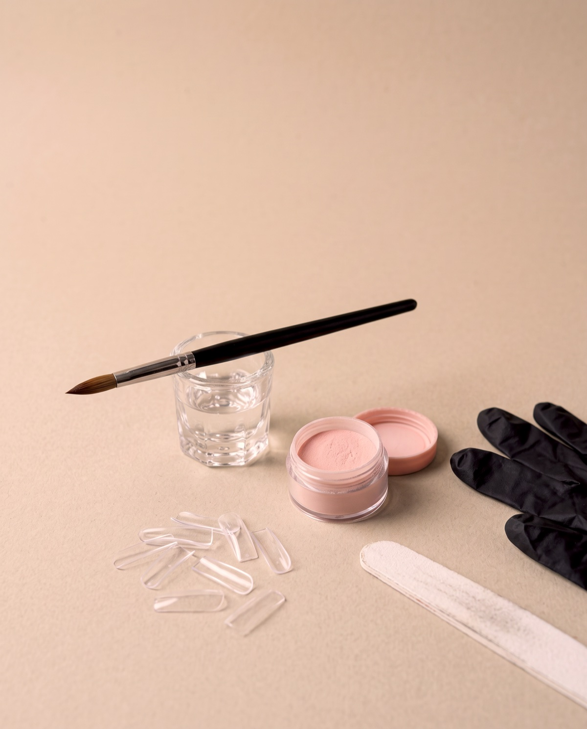 Mesa de trabajo de acrílico: pincel sobre un vaso de monómero, polvo acrílico, tips, lima y guantes negros